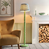 Endon Brenleigh floor lamp with green stacked sphere base and blue Ripple pleated shade, beside a mustard armchair and white fireplace with logs.