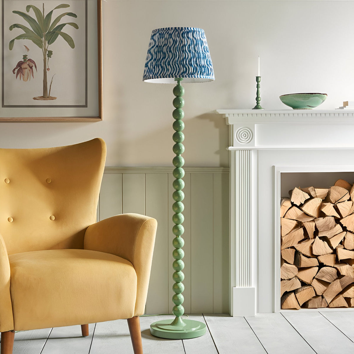 Endon Brenleigh floor lamp with stacked green gloss sphere base and blue Ripple pleated shade, beside a yellow armchair and white fireplace with logs.