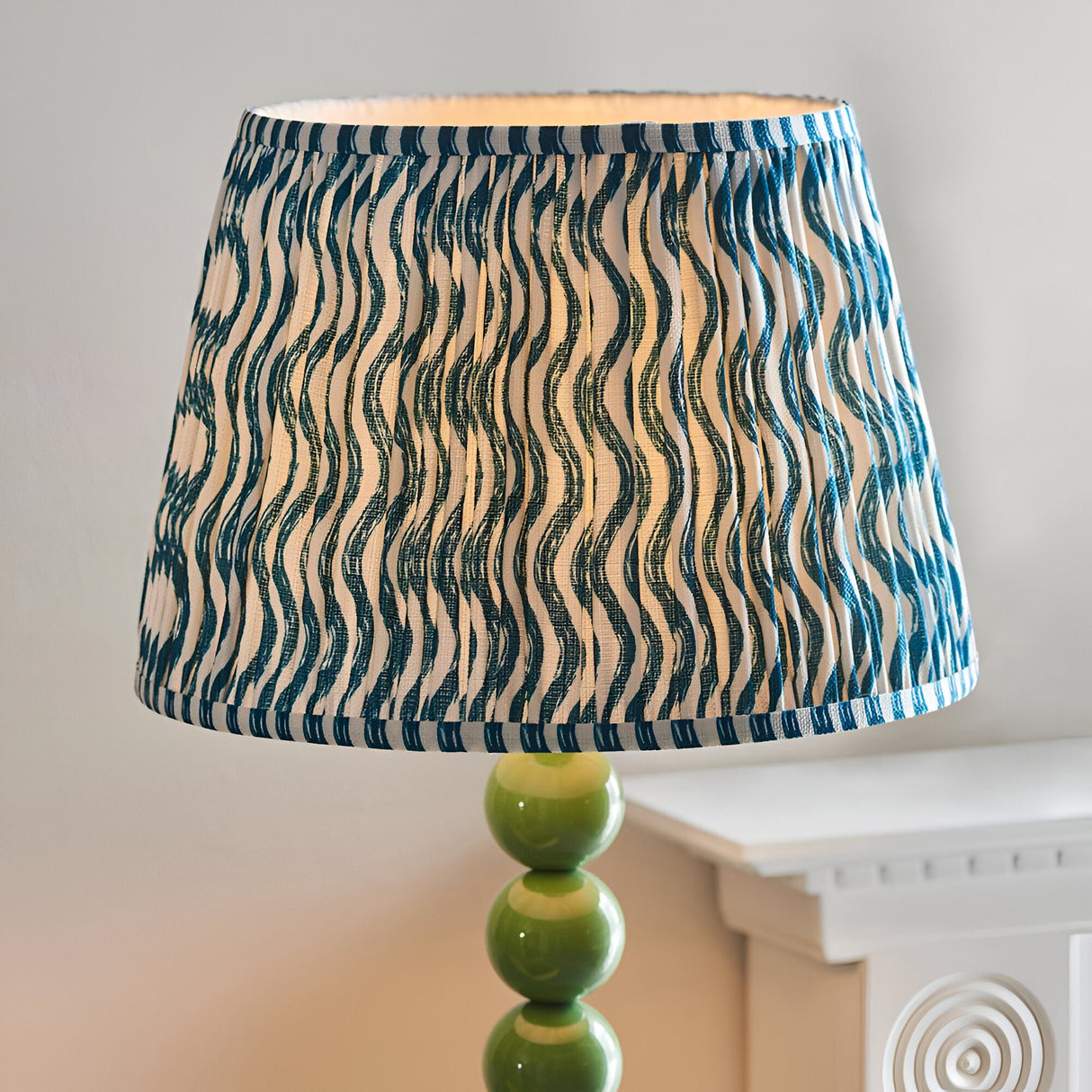Endon Brenleigh floor lamp detail showing green stacked sphere base and blue and white Ripple pleated faux linen shade beside a white mantel.