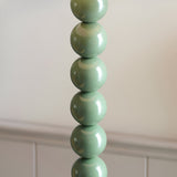 Endon Brenleigh Ripple floor lamp base close-up showing stacked glossy green spheres against a neutral wall with panelled cabinetry below.