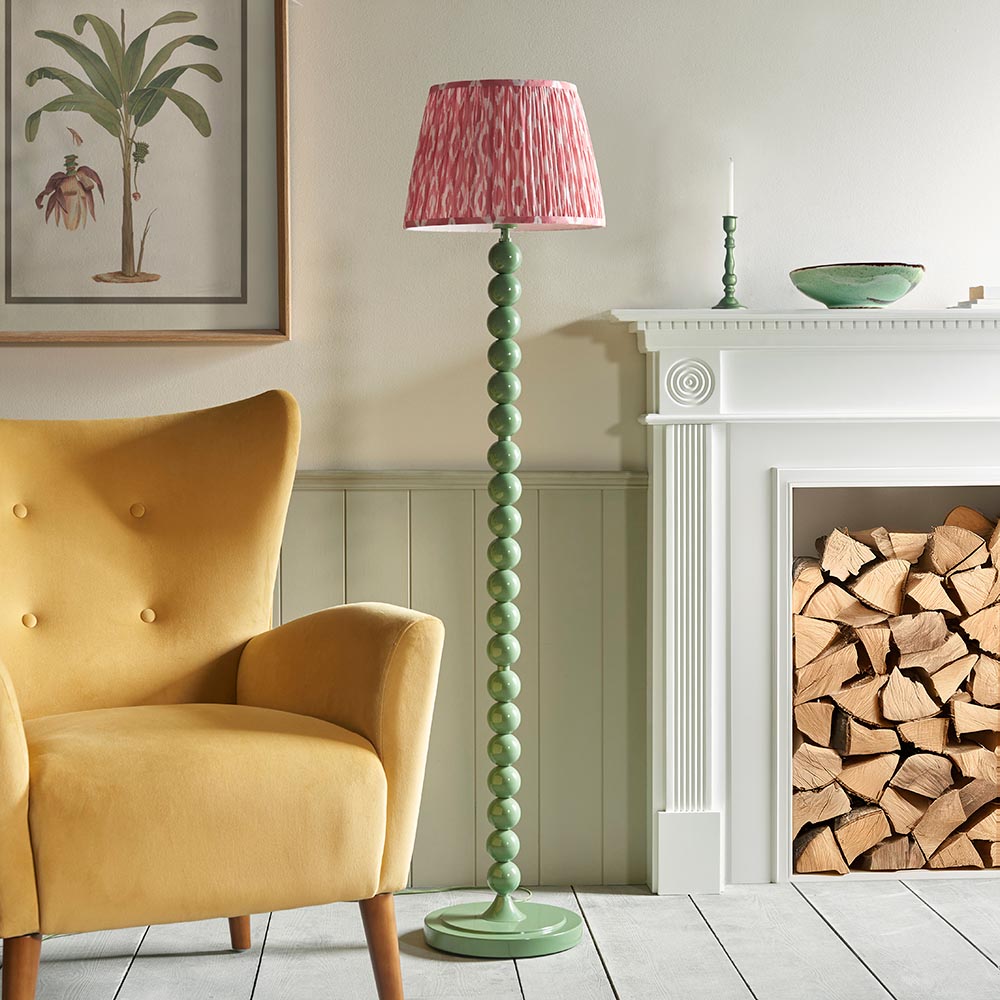 Brenleigh Ikat Floor Lamp with green stacked sphere base and pink patterned fabric shade, shown beside a fireplace and yellow armchair.