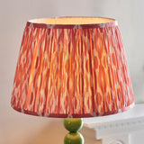 Brenleigh Ikat Floor Lamp with pleated pink and orange patterned fabric drum shade on a stacked green gloss sphere base, shown against a light background.