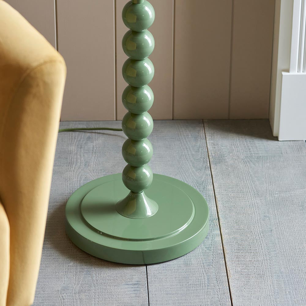 Brenleigh Ikat floor lamp base close-up, showing green gloss stacked sphere stem on a round green base, beside a mustard armchair on wood flooring.