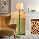 Endon Brenleigh Ivy floor lamp with stacked gloss green sphere base and tapered vintage white shade, beside a mustard armchair and log-store fireplace.