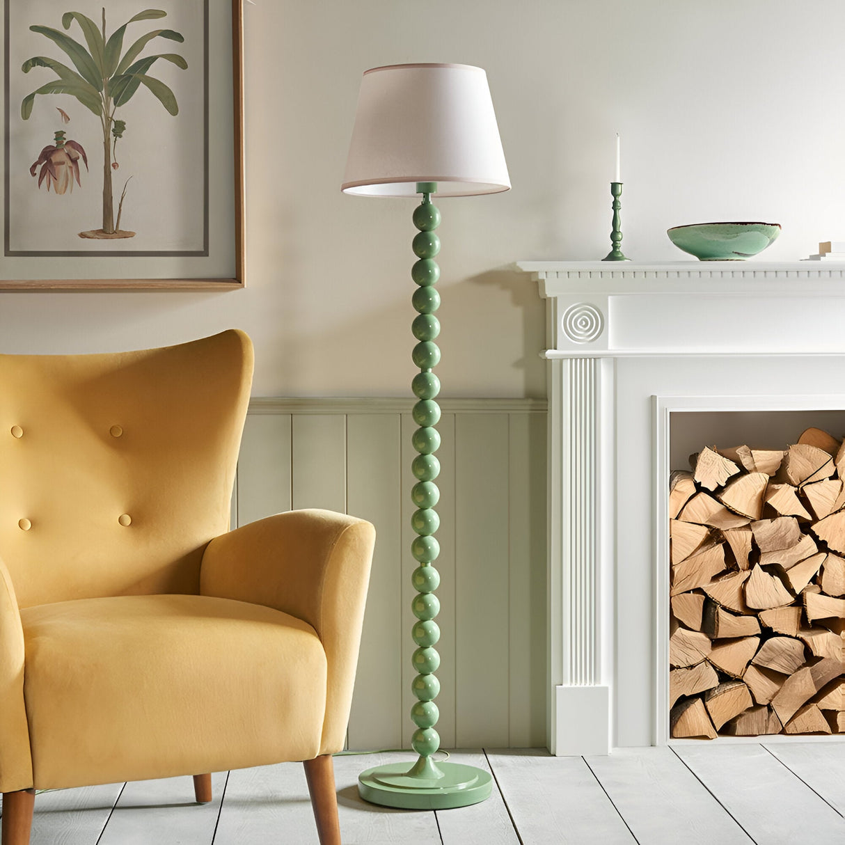 Endon Brenleigh Ivy floor lamp with glossy Cotswold green stacked sphere base and white tapered shade, beside a yellow armchair and white fireplace.