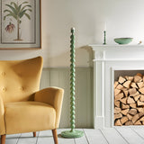 Endon Brenleigh floor lamp with a Cotswold green stacked sphere base beside a yellow armchair and white fireplace stacked with logs in a living room.