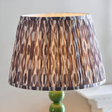 Endon Brenleigh floor lamp shade in grey Ikat pleated faux silk, set on a glossy green stacked sphere base beside a pale side table.