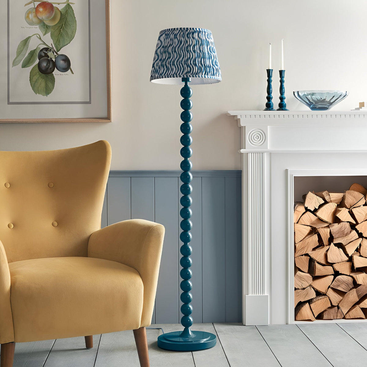 Endon Brenleigh stacked sphere floor lamp in marlin blue with a Ripple pleated shade, beside a yellow armchair and white fireplace with logs.