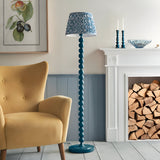 Endon Brenleigh stacked sphere floor lamp in marlin blue with a Ripple pleated shade, beside a yellow armchair and white fireplace with logs.