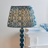 Endon Brenleigh floor lamp with stacked blue gloss sphere base and Ripple pleated shade in blue wave print, beside a white console with books.