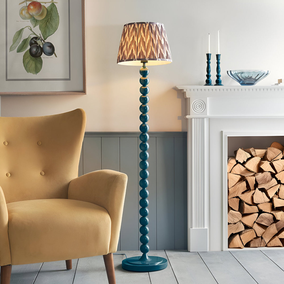 Brenleigh Zigzag Floor Lamp with teal stacked-sphere base and pleated zigzag-print shade, shown beside a mustard armchair in a living room setting.