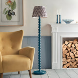 Brenleigh Zigzag Floor Lamp with stacked sphere blue gloss base and grey patterned pleated shade, shown beside a mustard armchair near a fireplace.