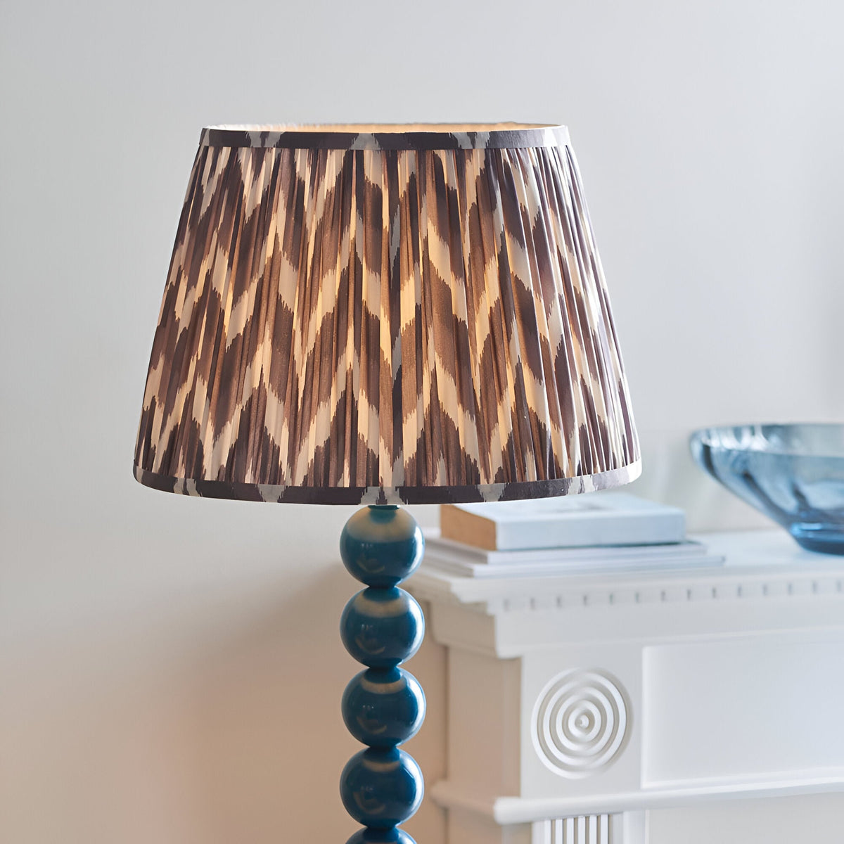 Brenleigh Zigzag Floor Lamp with stacked blue gloss sphere base and pleated grey zigzag-patterned fabric shade, shown beside a white fireplace mantel.