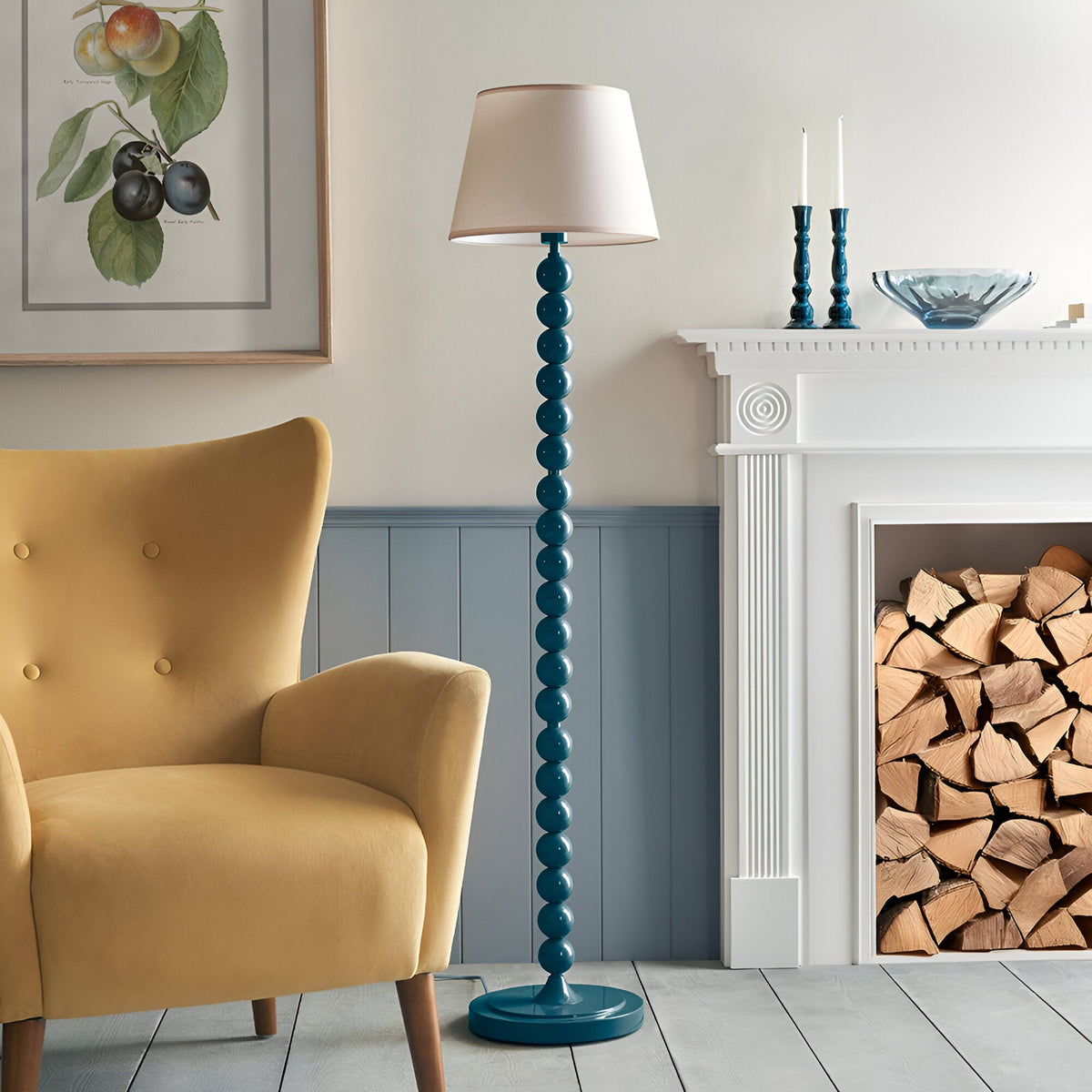 Brenleigh Ivy Floor Lamp with stacked sphere blue gloss base and tapered white fabric shade, shown beside a fireplace and yellow armchair.