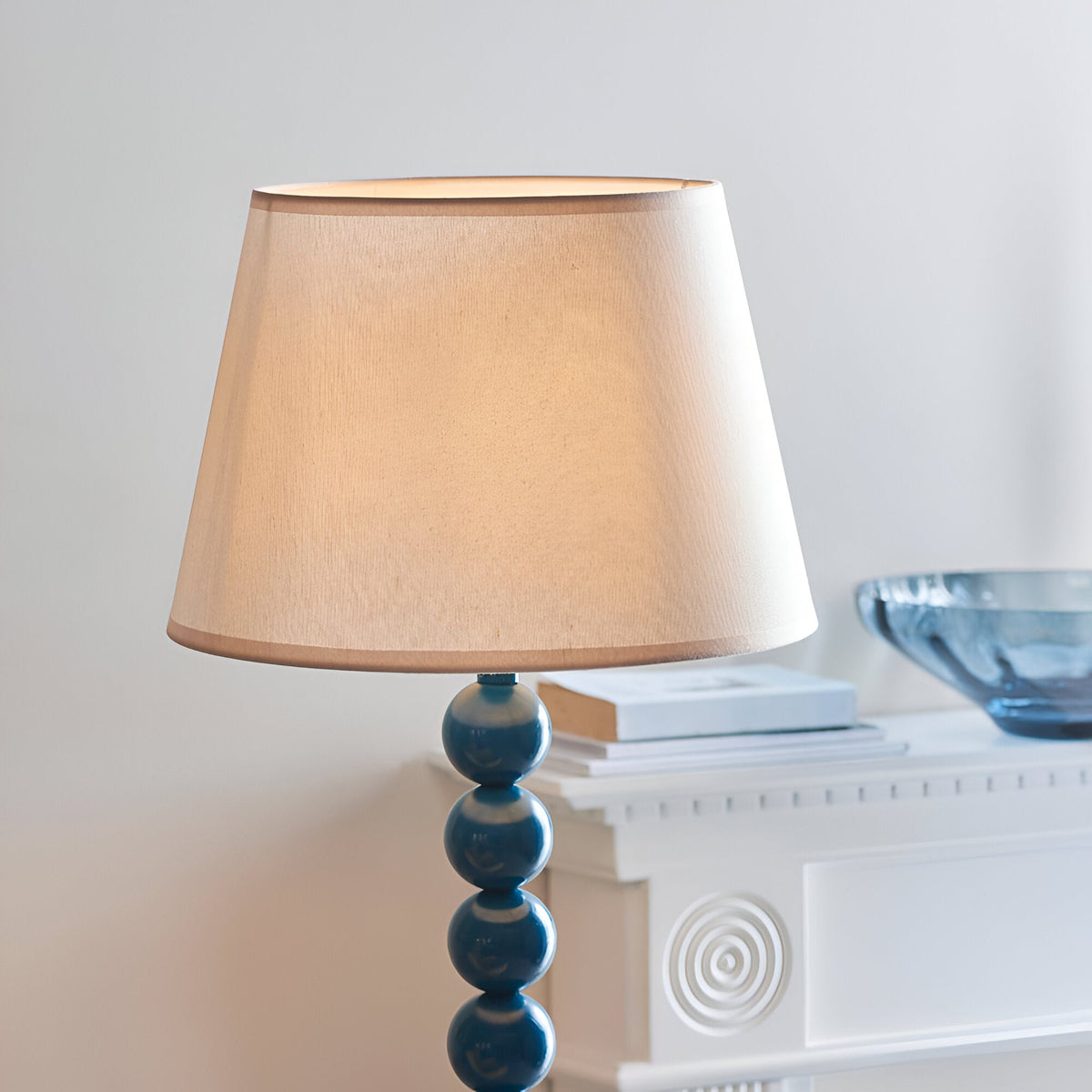 Brenleigh Ivy Floor Lamp with stacked blue gloss sphere base and tapered white fabric shade, shown beside a white console in a living room.