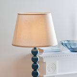 Brenleigh Ivy Floor Lamp with stacked blue gloss sphere base and tapered white fabric shade, shown beside a white console in a living room.