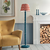 Endon Brenleigh Zigzag floor lamp in marlin blue with stacked sphere metal base and pleated pink zigzag shade, beside a yellow armchair and fireplace.