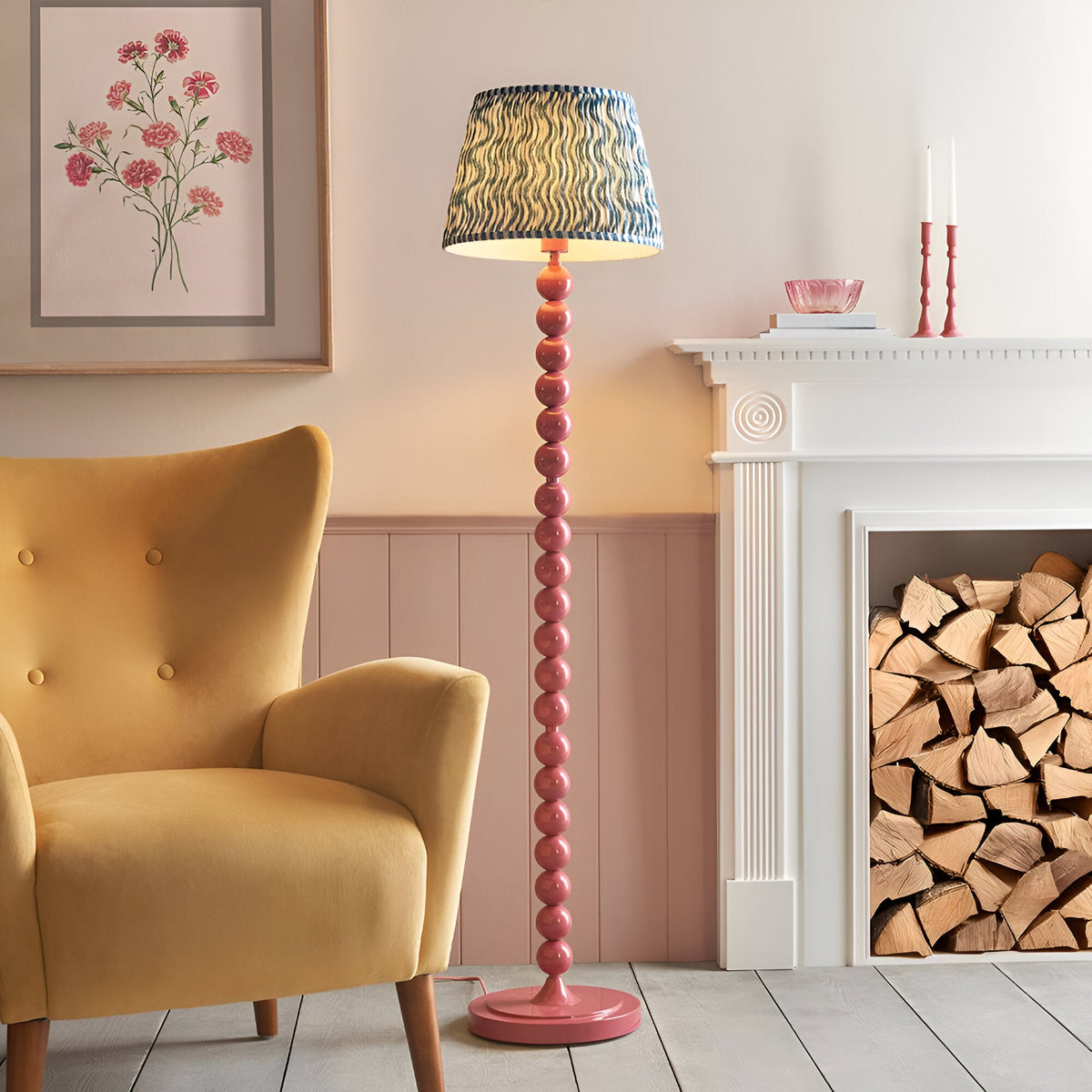 Endon Brenleigh floor lamp with pink stacked sphere base and blue Ripple pleated shade, beside a mustard armchair and white fireplace with logs.