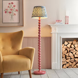 Endon Brenleigh floor lamp with pink stacked sphere base and blue Ripple pleated shade, beside a mustard armchair and white fireplace with logs.