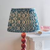 Endon Brenleigh floor lamp detail with pink clay glossy stacked sphere base and blue Ripple pleated faux linen shade beside a white mantelpiece.