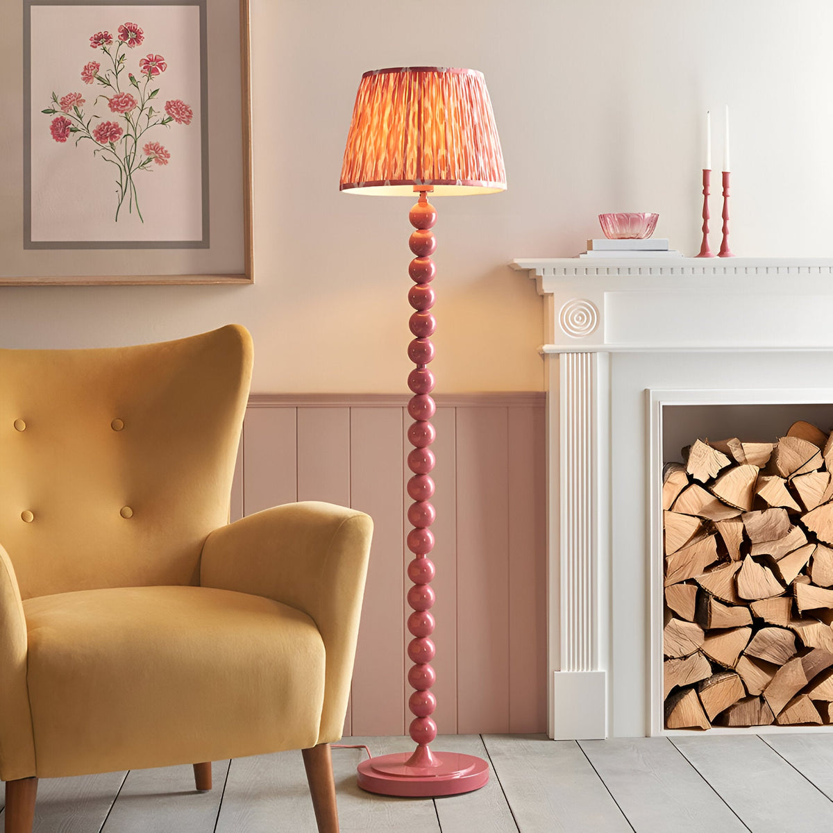 Endon Brenleigh floor lamp with pink stacked sphere base and pleated Ikat faux silk shade, beside a mustard armchair and white fireplace with logs.