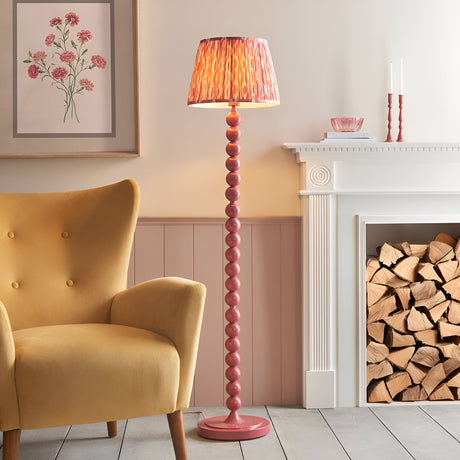 Endon Brenleigh floor lamp with pink stacked sphere base and pleated Ikat faux silk shade, beside a mustard armchair and white fireplace with logs.