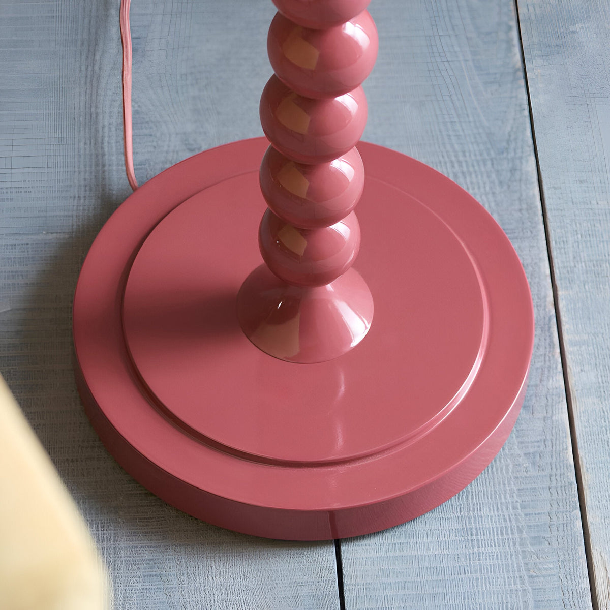 Close-up of the Endon Brenleigh floor lamp base in glossy pink clay, showing stacked spheres on a round plinth atop light grey wooden floorboards.