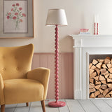 Endon Brenleigh Ivy floor lamp with glossy pink stacked sphere base and white tapered shade, beside a yellow armchair and white fireplace with logs.
