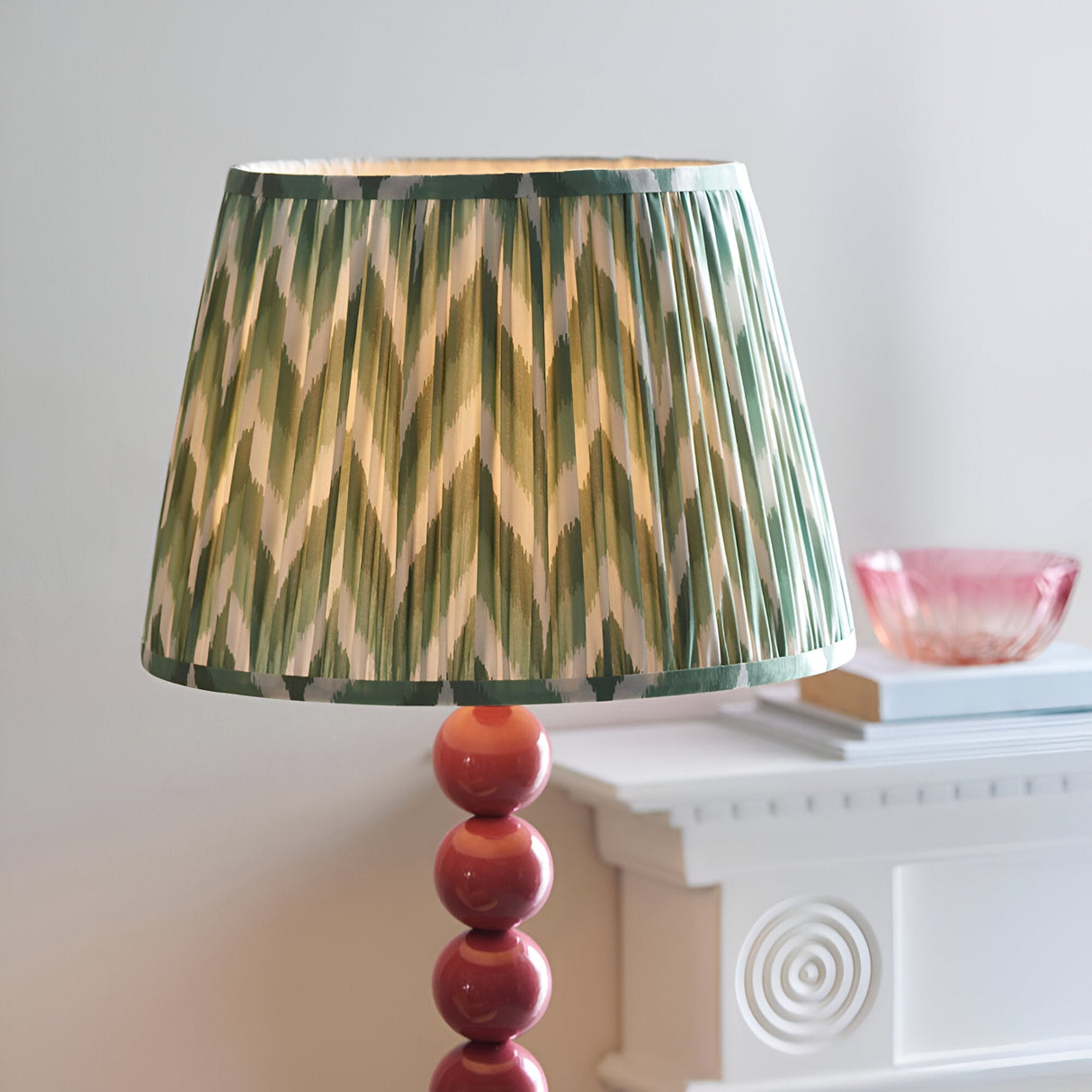Endon Brenleigh floor lamp with green zigzag pleated faux silk shade on a glossy pink stacked sphere base, beside a white mantel with a pink glass bowl.