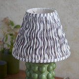 Endon Amberley Ripple table lamp with olive green ceramic bobble base and pleated grey wave-pattern fabric shade, shown on a wooden surface.
