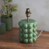 Endon Amberley Ripple table lamp base in gloss olive green ceramic with bobble texture and aged brass B22 holder, on a wooden surface beside plant pots.