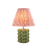 Amberley Ripple table lamp with a green ceramic bobble base, brass stem, and pink and orange wavy-pattern fabric shade on a white background.