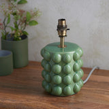 Amberley Ripple table lamp base in green ceramic with bobble texture and aged brass B22 lamp holder, shown without shade on a wooden surface.
