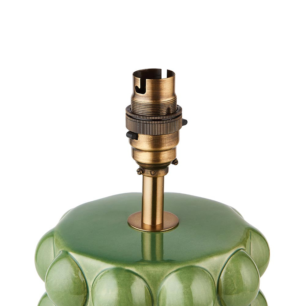Close-up of the Amberley Ripple Table Lamp's aged brass B22 switched lamp holder atop a green ceramic bobble base, on a white background.
