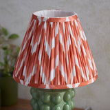 Endon Amberley table lamp with pleated apricot orange and white zigzag fabric shade on a glossy green bobble ceramic base, shown on a console.