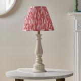 Endon Carlworth Ikat table lamp in almond gloss resin spindle base with pleated coral and white Ikat shade, on a marble side table by a mirror.