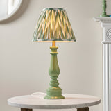 Carlworth Zigzag Table Lamp with green resin spindle base and pleated green zigzag-patterned shade, shown lit on a marble side table.