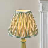 Carlworth Zigzag Table Lamp with pleated green, cream and gold patterned shade on a glossy green spindle-style resin base, set against a light background.