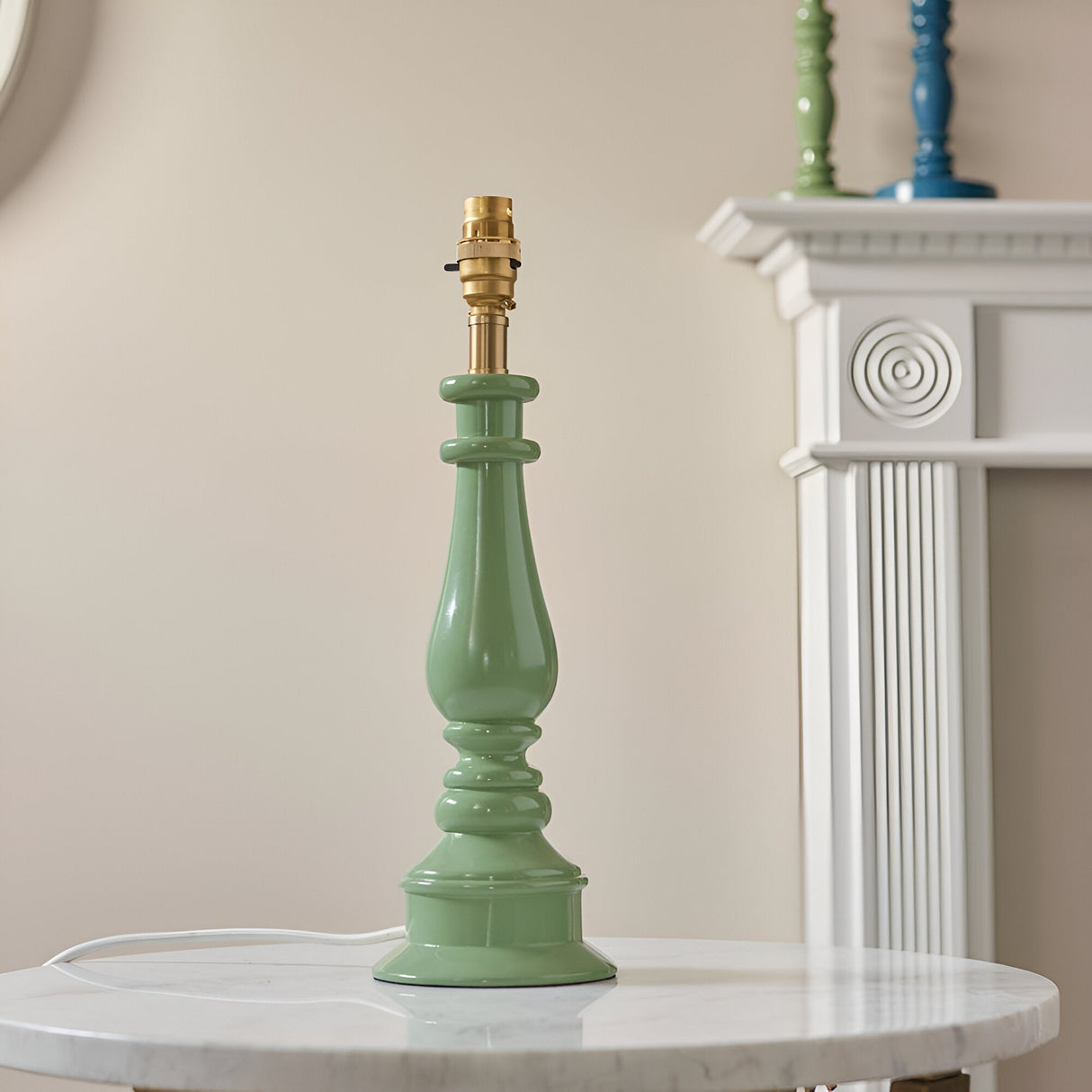 Carlworth Zigzag Table Lamp base in Cotswold Green resin with turned spindle column and brass fitting, shown shadeless on a marble table near a white mantel.