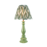 Carlworth Zigzag Table Lamp with a green resin spindle base and a pleated zigzag-patterned shade in green, cream and gold, shown on a plain white background.