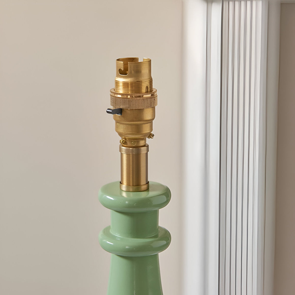 Carlworth Zigzag Table Lamp in Cotswold Green, close-up of the turned resin base with brass B22 bulb holder and switch, shown against a neutral wall.