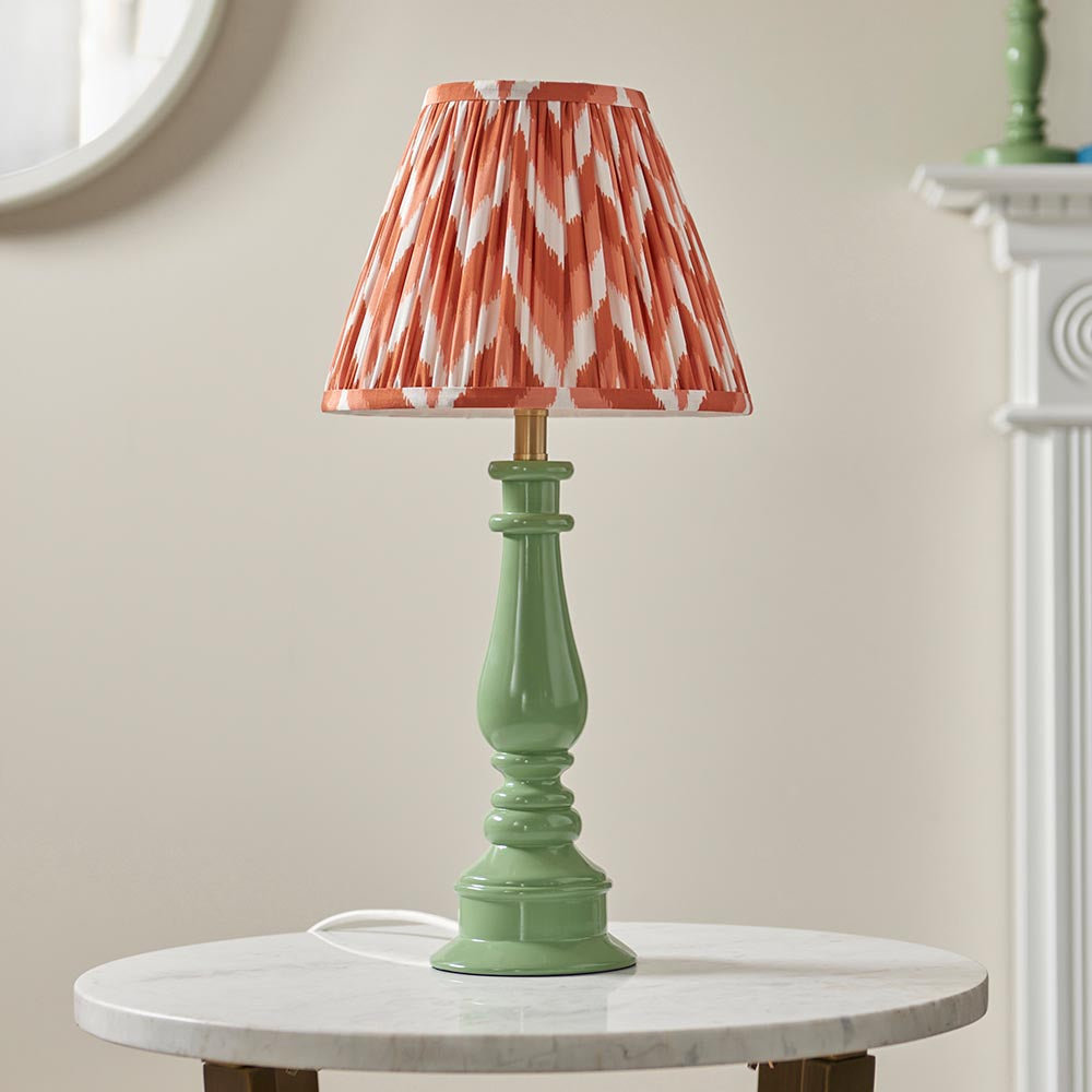 Carlworth Zigzag Table Lamp with a green spindle-style resin base and pleated apricot zigzag-print shade, shown on a marble side table.