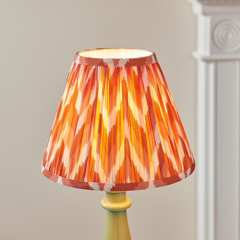 Carlworth Zigzag Table Lamp with green resin spindle base and pleated orange zigzag-pattern shade with taped edges, set against a neutral background.