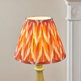 Carlworth Zigzag Table Lamp with green resin spindle base and pleated orange zigzag-pattern shade with taped edges, set against a neutral background.
