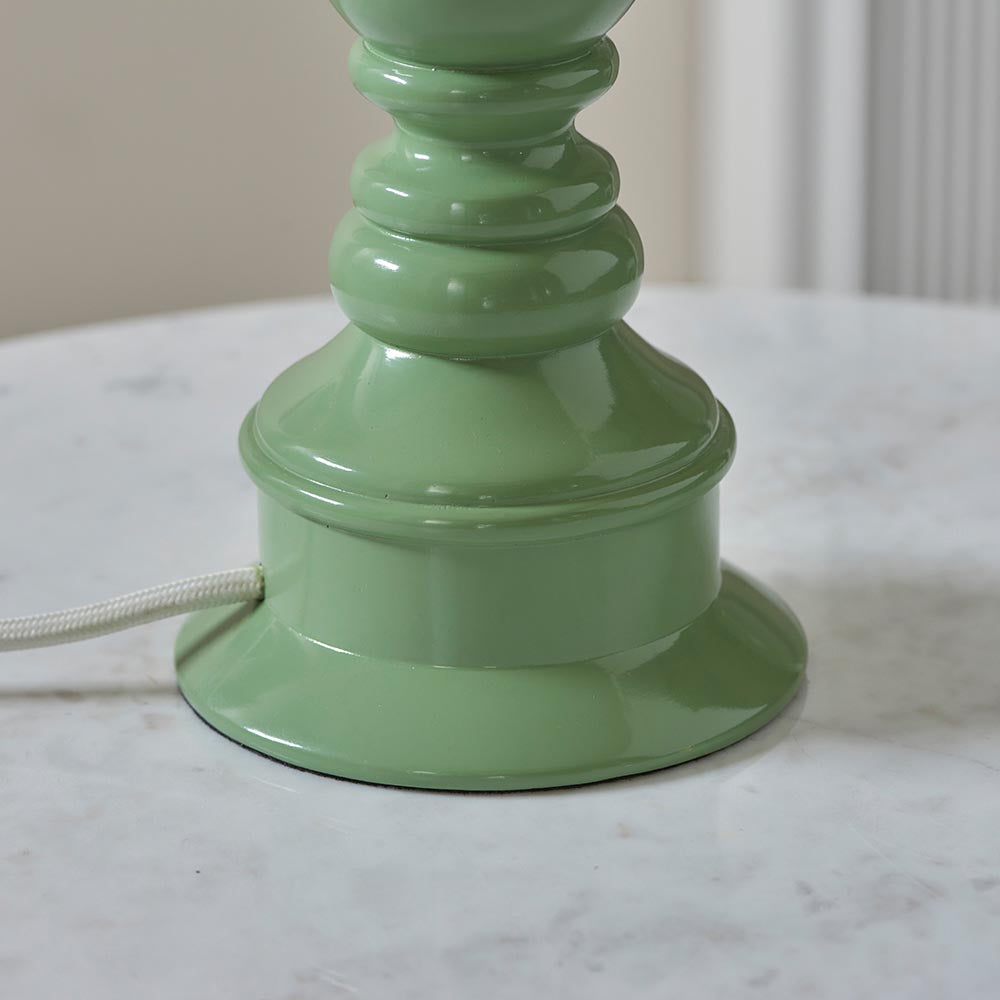Close-up of the Carlworth table lamp base in glossy green resin with a turned spindle design and white cable, shown on a marble surface.