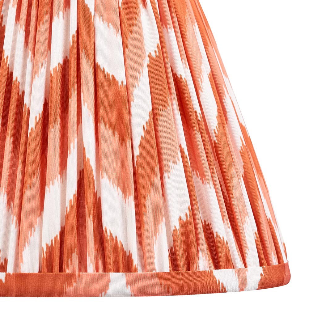 Close-up of the Carlworth table lamp's pleated Zigzag shade in apricot and white faux silk with a taped trim edge and tapered shape.