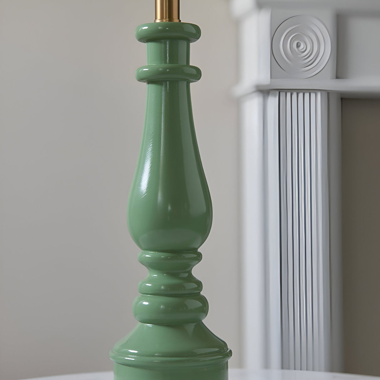 Close-up of the Endon Carlworth Ivy table lamp's turned green resin spindle base with brass lamp holder, beside a white fluted column.
