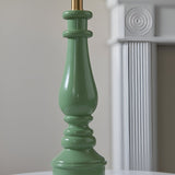 Close-up of the Endon Carlworth Ivy table lamp's turned green resin spindle base with brass lamp holder, beside a white fluted column.