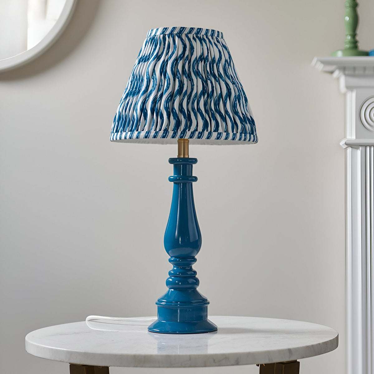 Carlworth Ripple Table Lamp in glossy blue resin with turned spindle base and pleated blue and white patterned shade, shown on a marble side table.