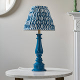 Carlworth Ripple Table Lamp in glossy blue resin with turned spindle base and pleated blue and white patterned shade, shown on a marble side table.